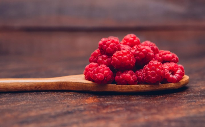 Red raspberries in a wooden spoon side view on a wooden background