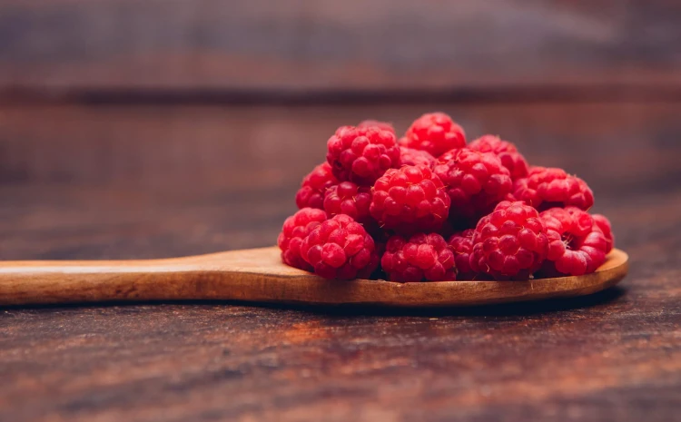 Red raspberries in a wooden spoon side view on a wooden background